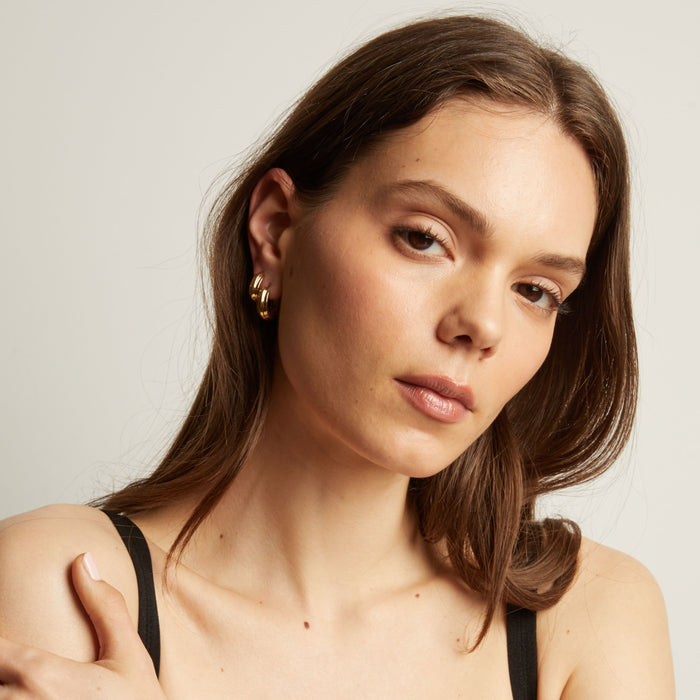 Model. Woman with long brown hair wearing gold earrings against a neutral background.
