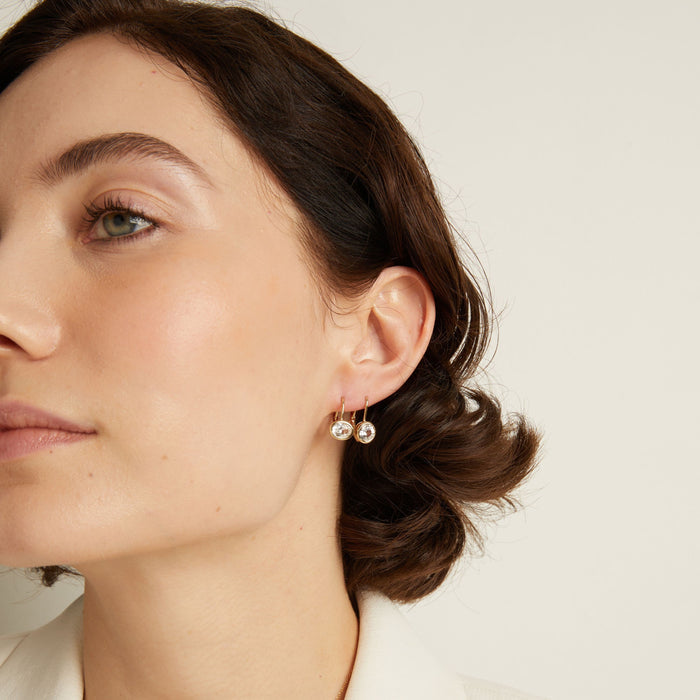 Model. Close-up of a woman wearing gemstone hoop earrings with a neutral background