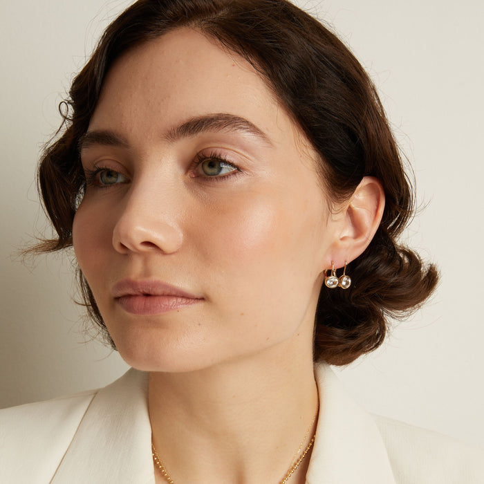 Model. Close-up of a woman wearing gemstone hoop earrings with a neutral background