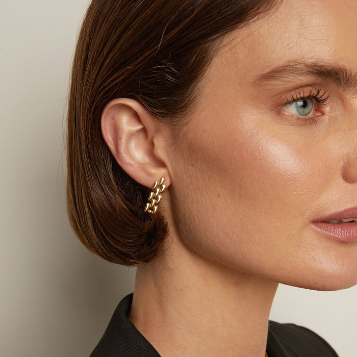 Model. Close-up of a woman wearing gold chain earrings with a neutral background