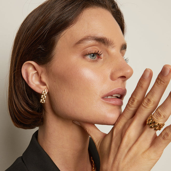 Model. Close-up of a woman wearing gold chain earrings with a neutral background