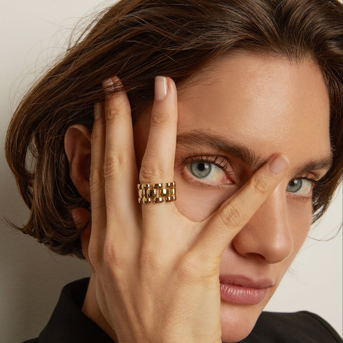 Model. Close-up of a person with a gold ring on their finger, touching their face.