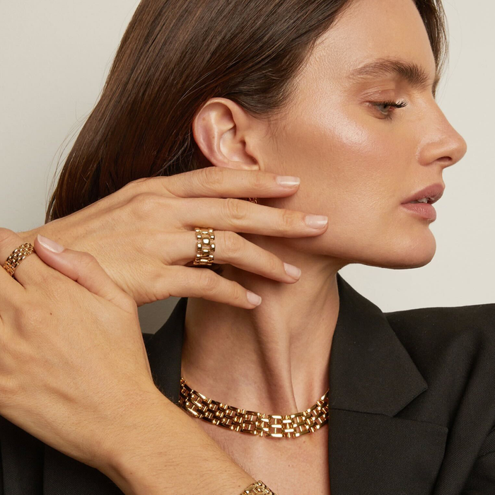 Model. Woman wearing gold jewelry including a bracelet and ring, with a neutral background