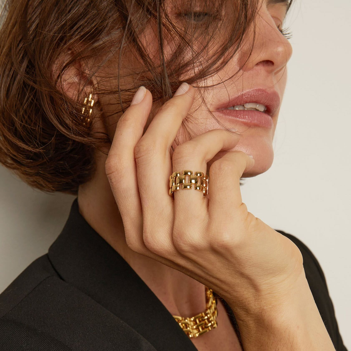 Close-up of a person wearing gold jewelry including earrings, ring, and bracelet.