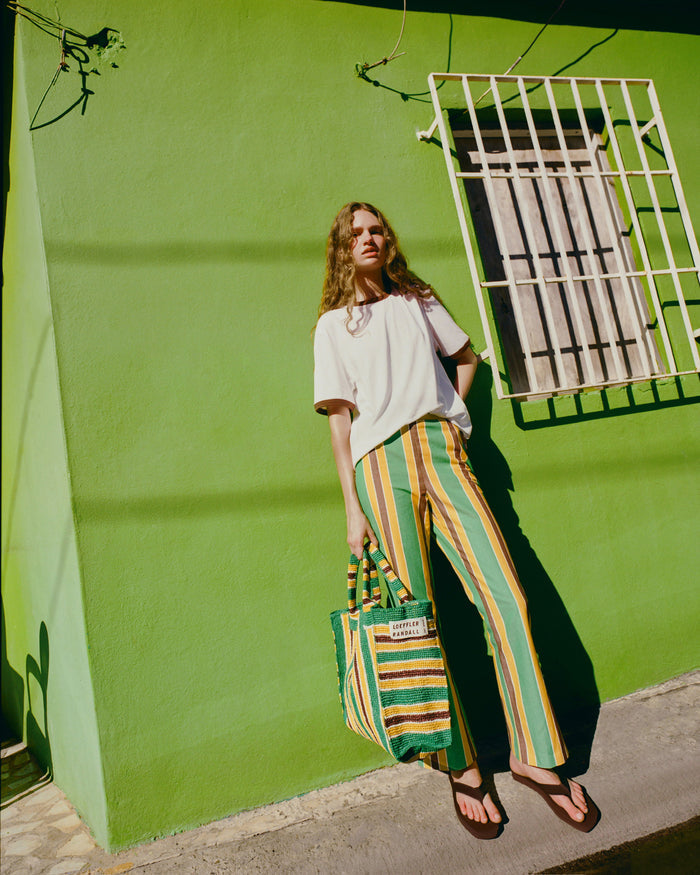 Pasha Trouser in green/yellow/brown striped cotton-linen, Harly Tee in white cotton, Chase Brown Flip Flop, and Sol Green/Yellow Crochet Beach Tote.