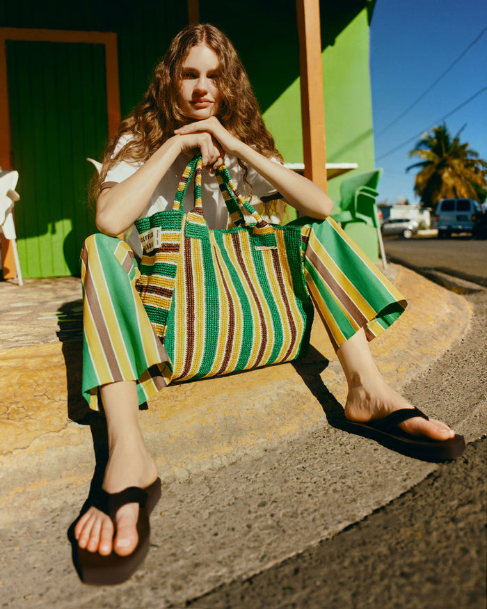 Pasha Trouser in green/yellow/brown striped cotton-linen, Harly Tee in white cotton, Chase Brown Flip Flop, and Sol Green/Yellow Crochet Beach Tote.