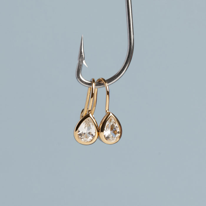 Model. Gold teardrop earrings on a fishing hook against a light blue background