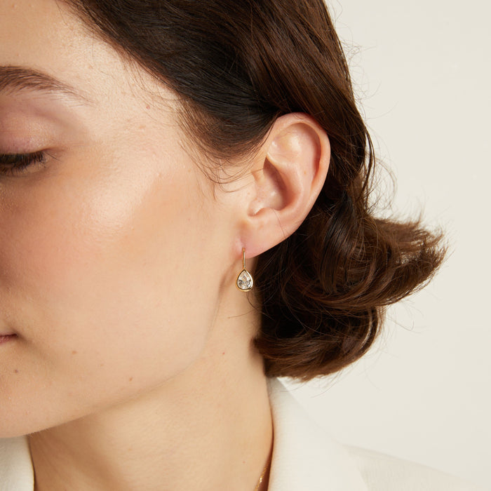 Model. Close-up of a woman wearing gemstone hoop earrings with a neutral background