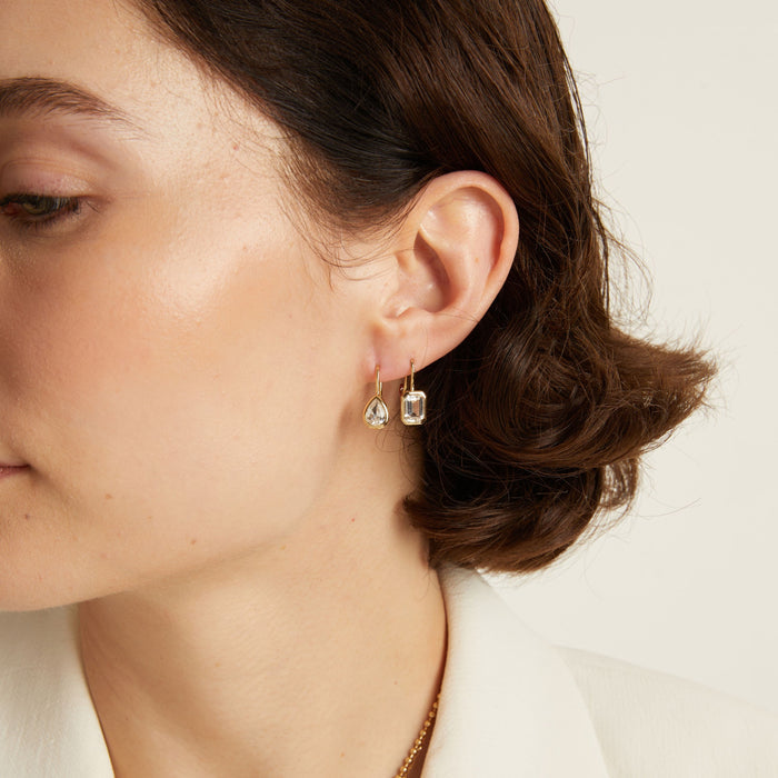 Model. Close-up of a woman wearing gemstone hoop earrings with a neutral background