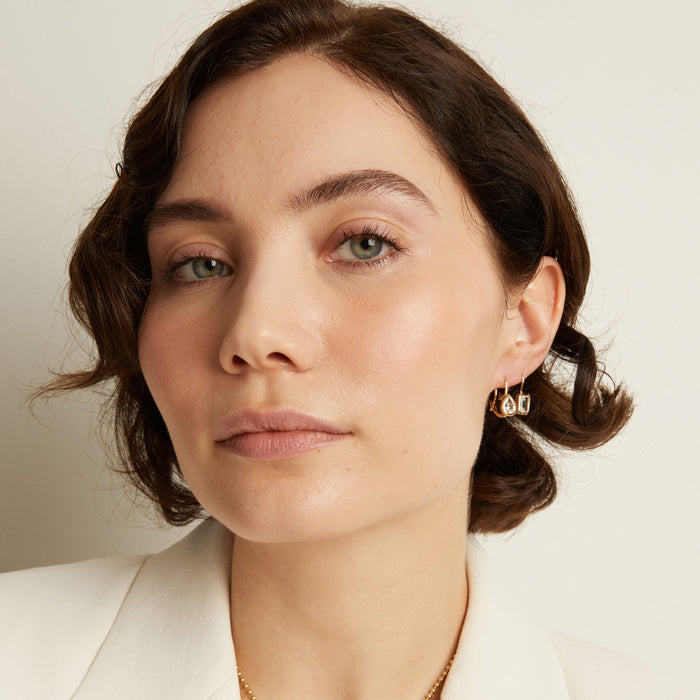 Model. Close-up of a woman wearing gemstone hoop earrings with a neutral background