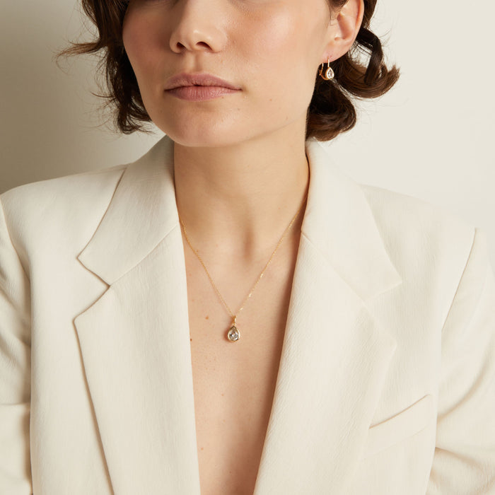Model. Woman wearing a white blazer and a delicate necklace with a small pendant.
