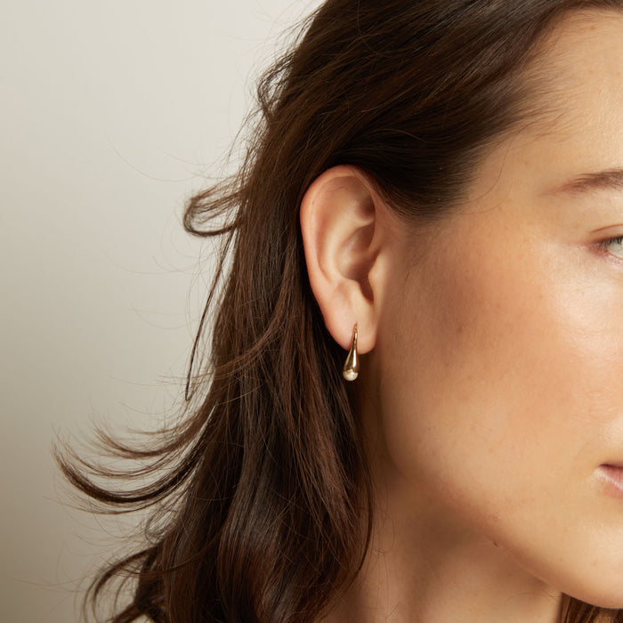 Model Close-up of a person wearing a gold earring with a neutral background