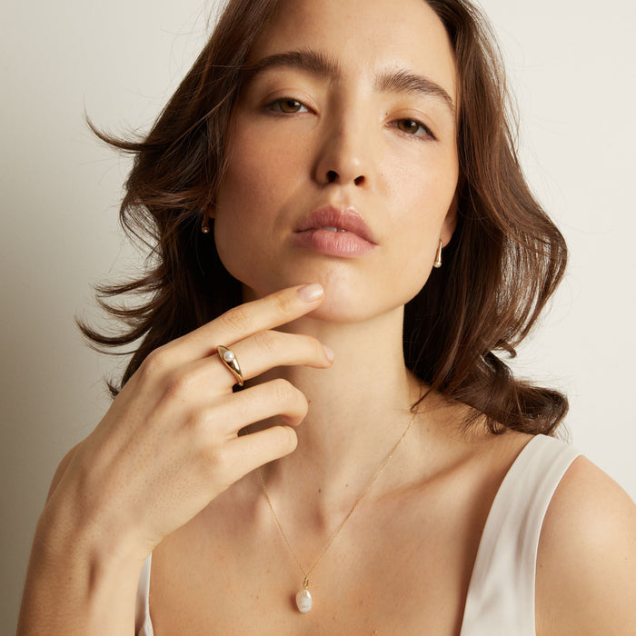 Model Woman wearing a pearl necklace and ring against a neutral background