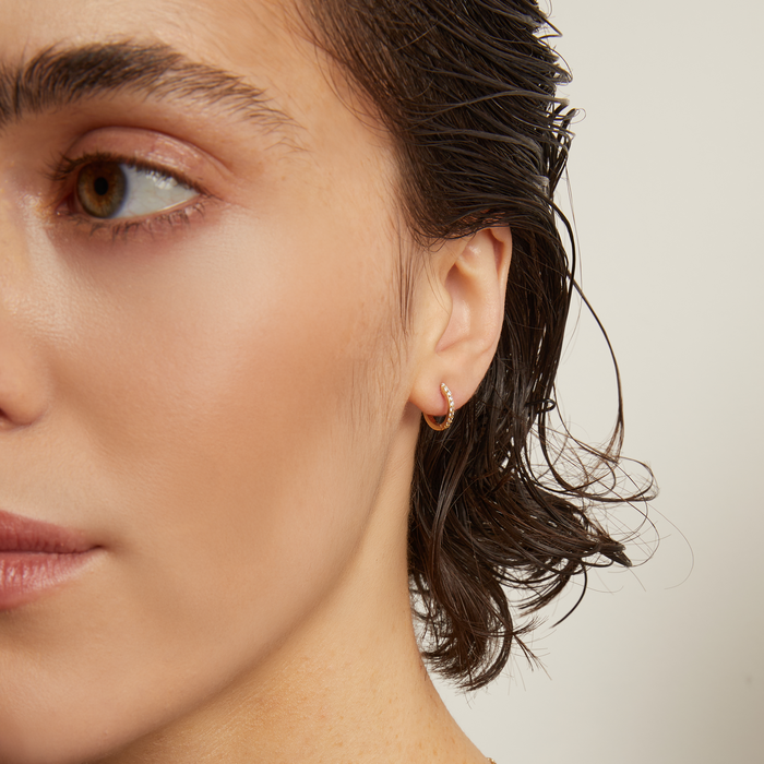 Model. Close-up of a person wearing a gold earring and necklace against a neutral background