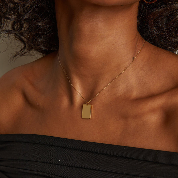 Model. Close-up of a person wearing a gold necklace with a tag pendant.