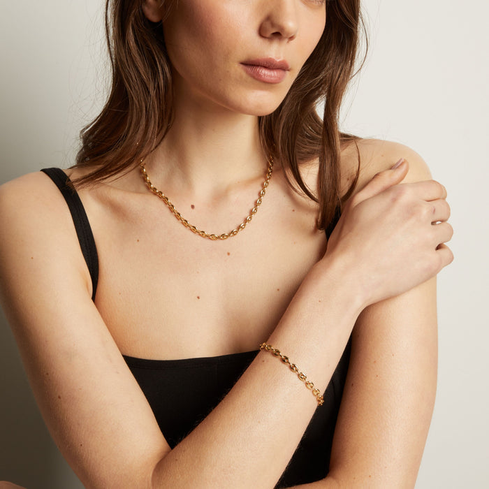 Gold chain necklace and bracelet on woman in black tank top. Model
