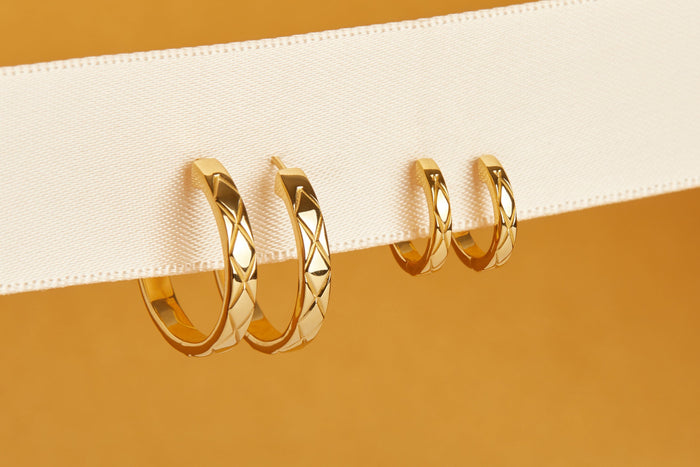 Flatlay Model Close-up of two pairs of gold quilted huggie earrings resting on a split white and orange surface