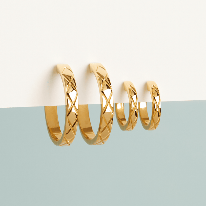 Flatlay Model Close-up of two pairs of gold quilted earrings on a split white and light blue background