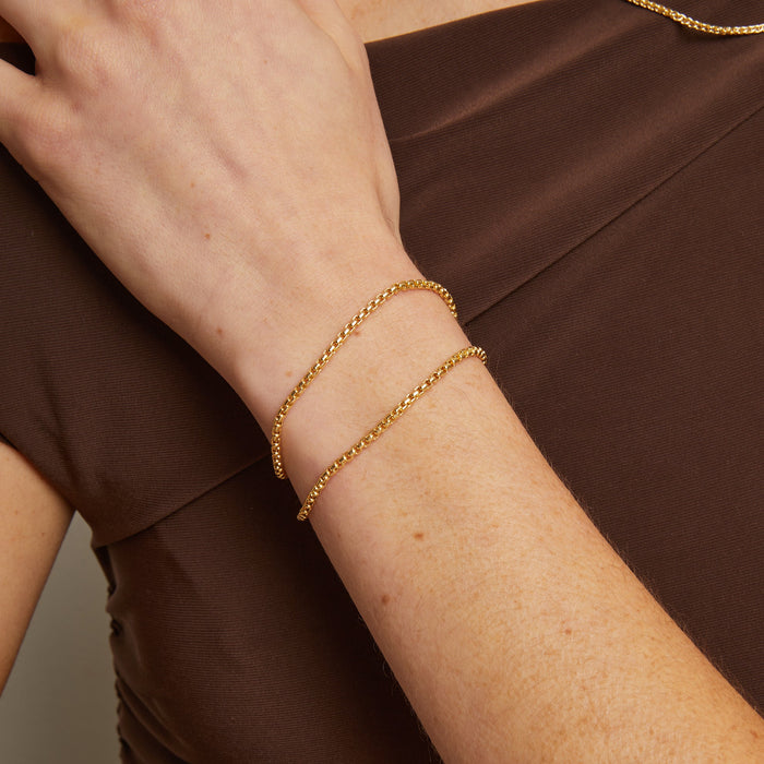 Model. Gold bracelet on a wrist against a brown background