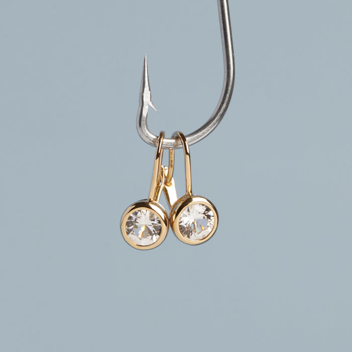 Model. Gold earrings with clear gemstones on a gray background
