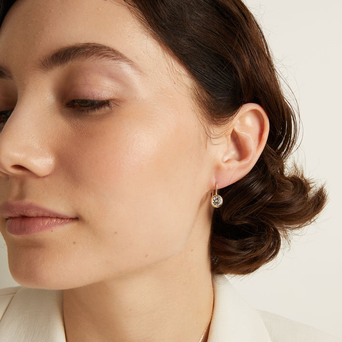 Model. Close-up of a woman wearing gemstone hoop earrings with a neutral background