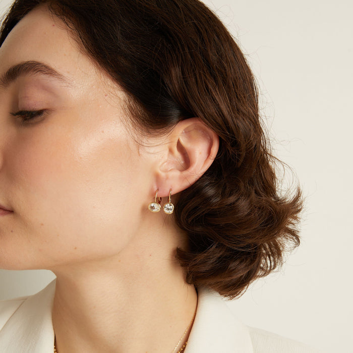 Model. Close-up of a woman wearing gemstone hoop earrings with a neutral background