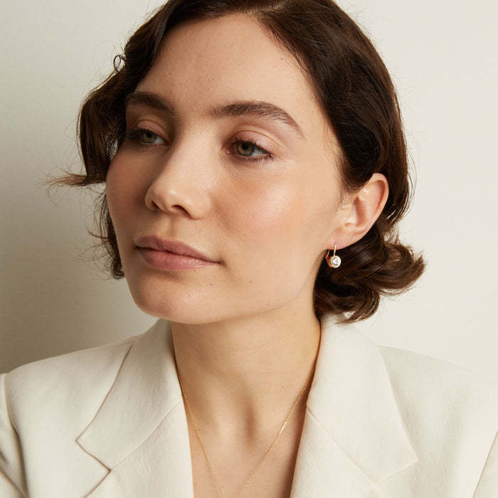 Model. Close-up of a woman wearing gemstone hoop earrings with a neutral background