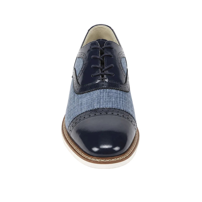 A men's cap-toe oxford shoe featuring a glossy sapphire blue patent leather toe cap and laces, a light blue denim-textured side panel, and a brown and white welted sole, shown from a front-facing perspective on a white background.