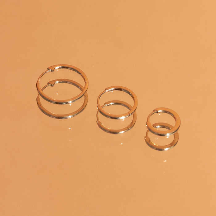 Flatlay Model Close-up of three pairs of gold hoop earrings on an orange background.