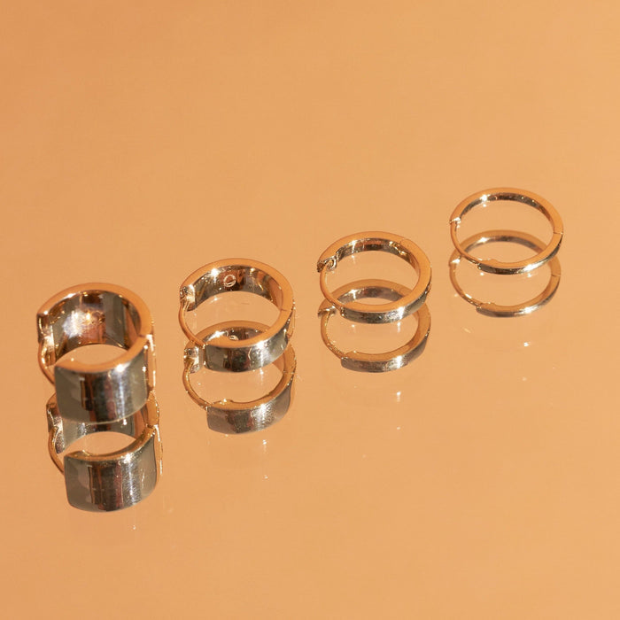 Flatlay Model Close-up of three pairs of gold hoop earrings on an orange background.