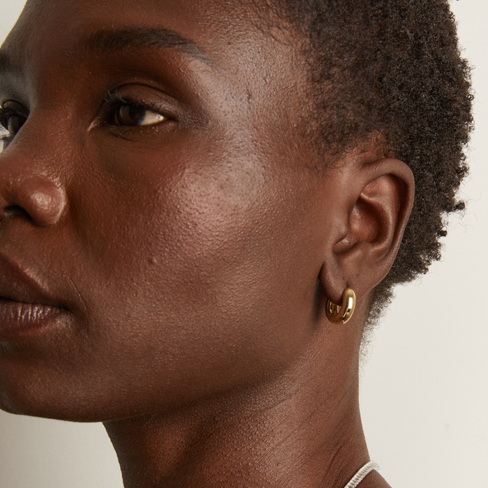 Model. Close-up of a person wearing a gold hoop earring against a neutral background