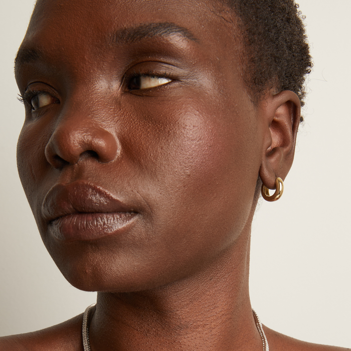 Model. Close-up of a person wearing a gold hoop earring against a neutral background