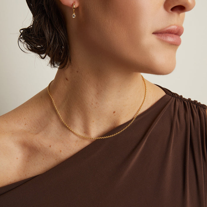 Model. Close-up of a person wearing a gold necklace and earring against a neutral background