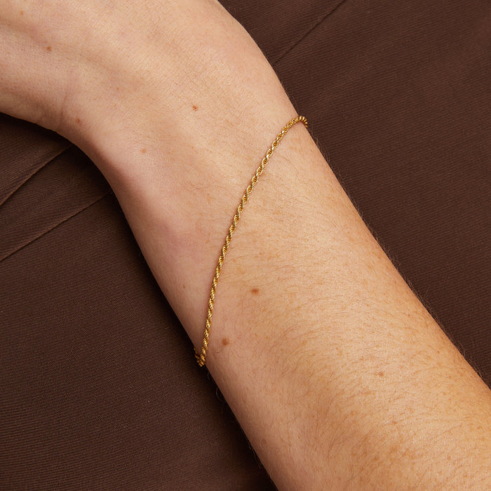 Model. Gold bracelet on a person's wrist against a brown background
