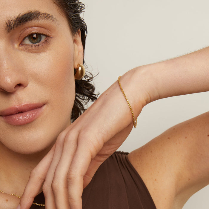 Model. Woman wearing gold jewelry including earrings and a bracelet on a neutral background