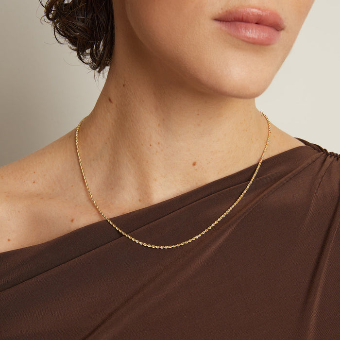 Model. Close-up of a person wearing a gold necklace with a neutral background