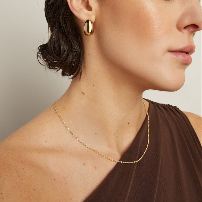 Model. Close-up of a woman wearing gold earrings and a necklace against a neutral background