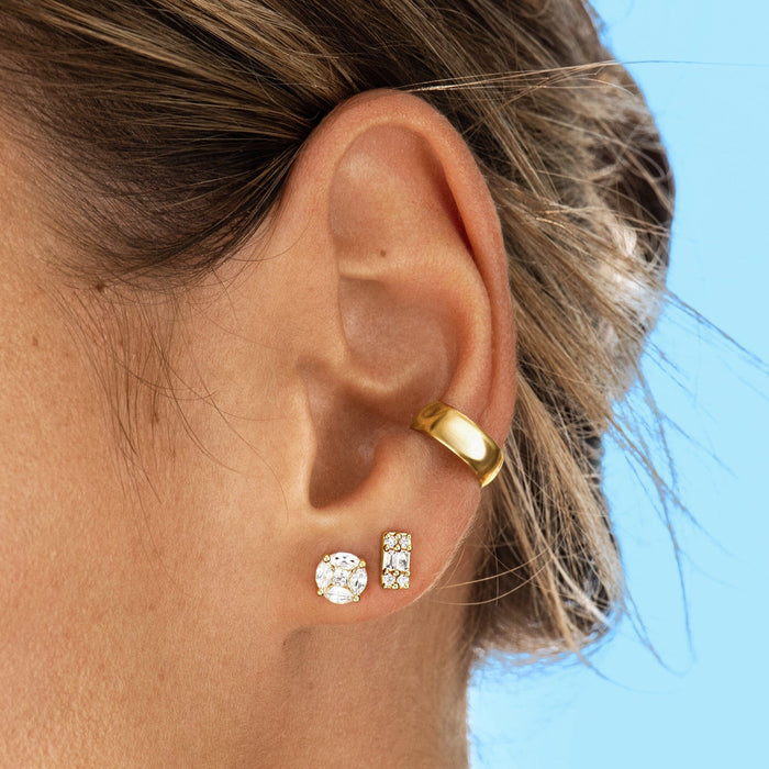 Model. Close-up of an ear wearing gold hoop earrings with a blurred blue background