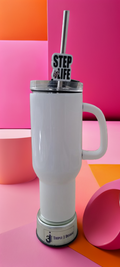 A white insulated travel tumbler with a handle, clear lid, and metal straw. The straw has a black and white 'STEP OR LIFE' sign attached.