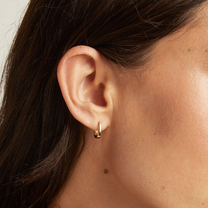Model. Close up of woman's ear with gold huggie earring.