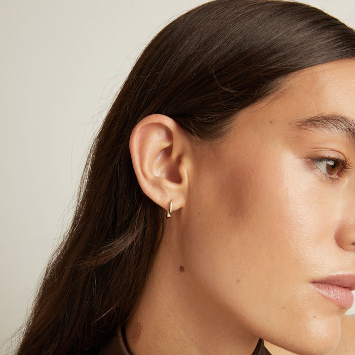 Model. Close up of woman wearing gold huggie earring.