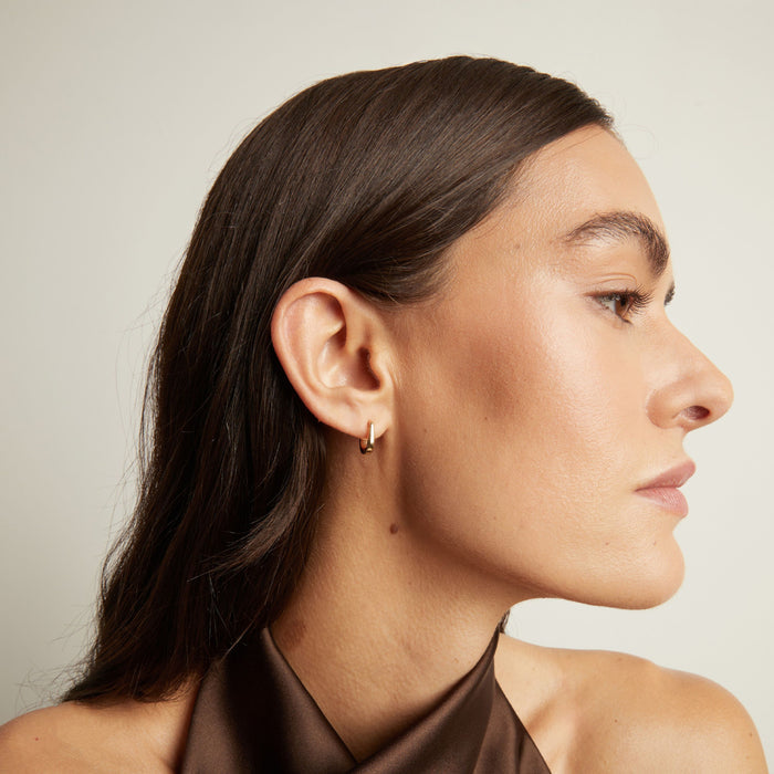 Model. Close up of woman wearing gold huggie earring.
