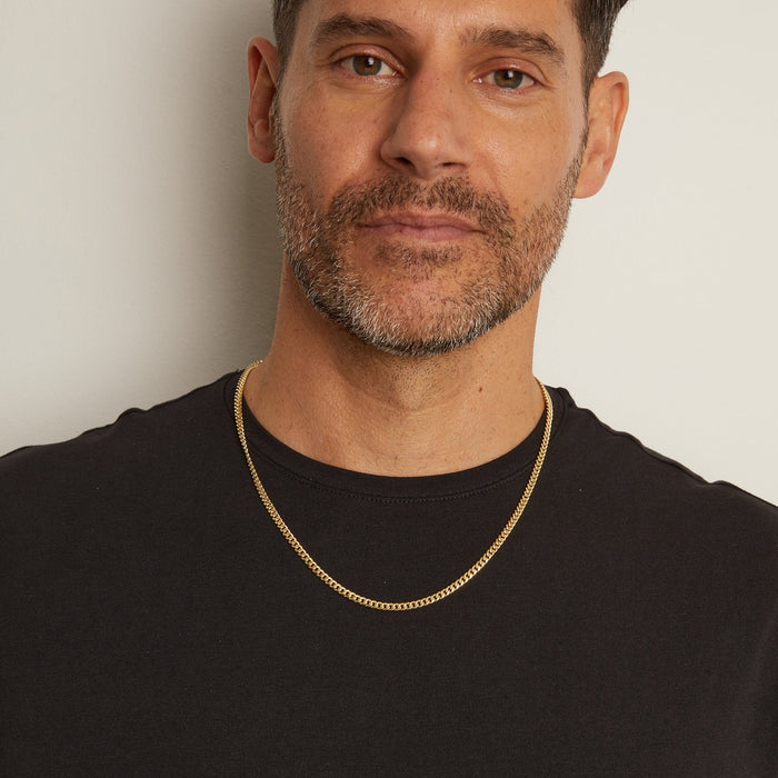 Man wearing a black shirt and gold chain necklace against a plain background