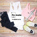 A flat-lay of athletic apparel on a wood plank background: a white racerback tank top with a periodic-table-style 'Fe male' graphic and text, a pink sports bra with a visible Nike swoosh, black leggings with white Nike text, a clear tumbler with a green straw, and white sneakers.