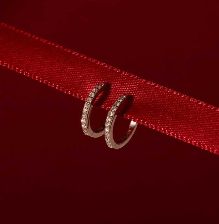 Flatlay Model Close-up of a pair of gold and diamond hoop earrings on a red ribbon