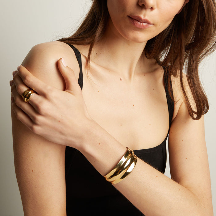 Model. Woman wearing a gold bracelet and ring on a neutral background