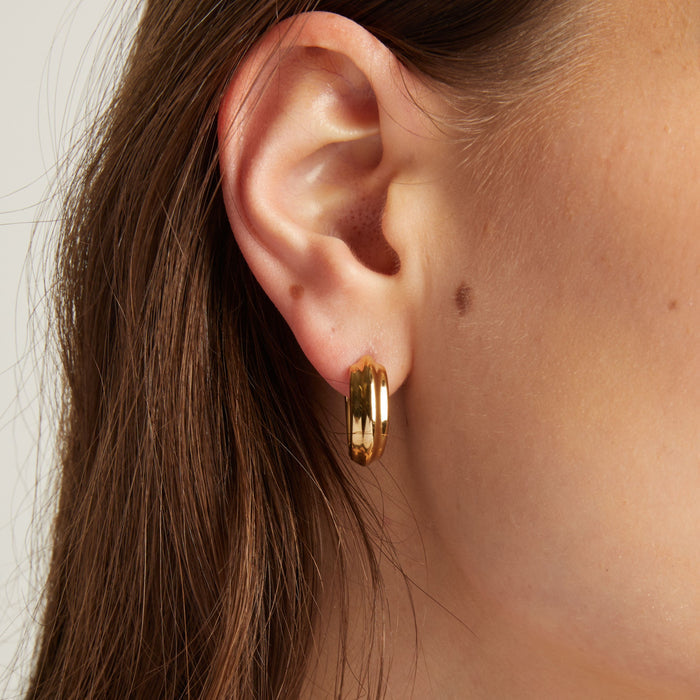 Model. Gold hoop earring worn by a person with brown hair.