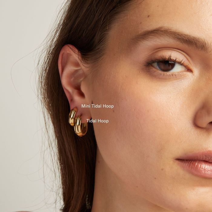 Model. Close up of a person wearing gold hoop earrings with a neutral background