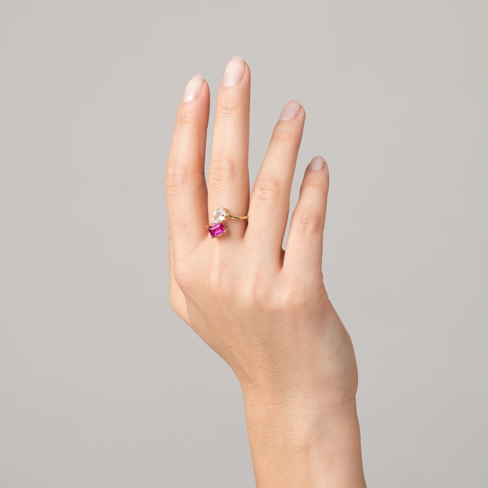 Model. Hand wearing a ring with a pink gemstone on a gray background