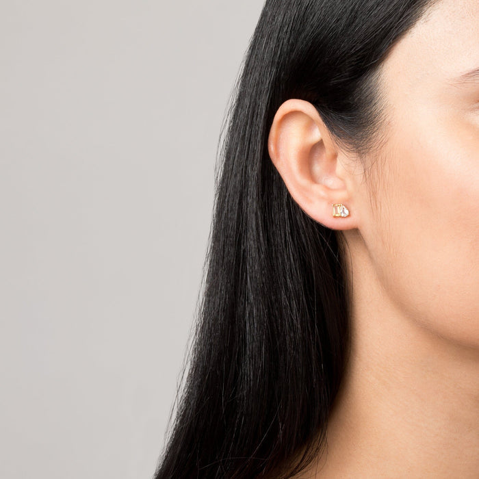 Model. Close-up of an ear wearing a gold earring with a gray background